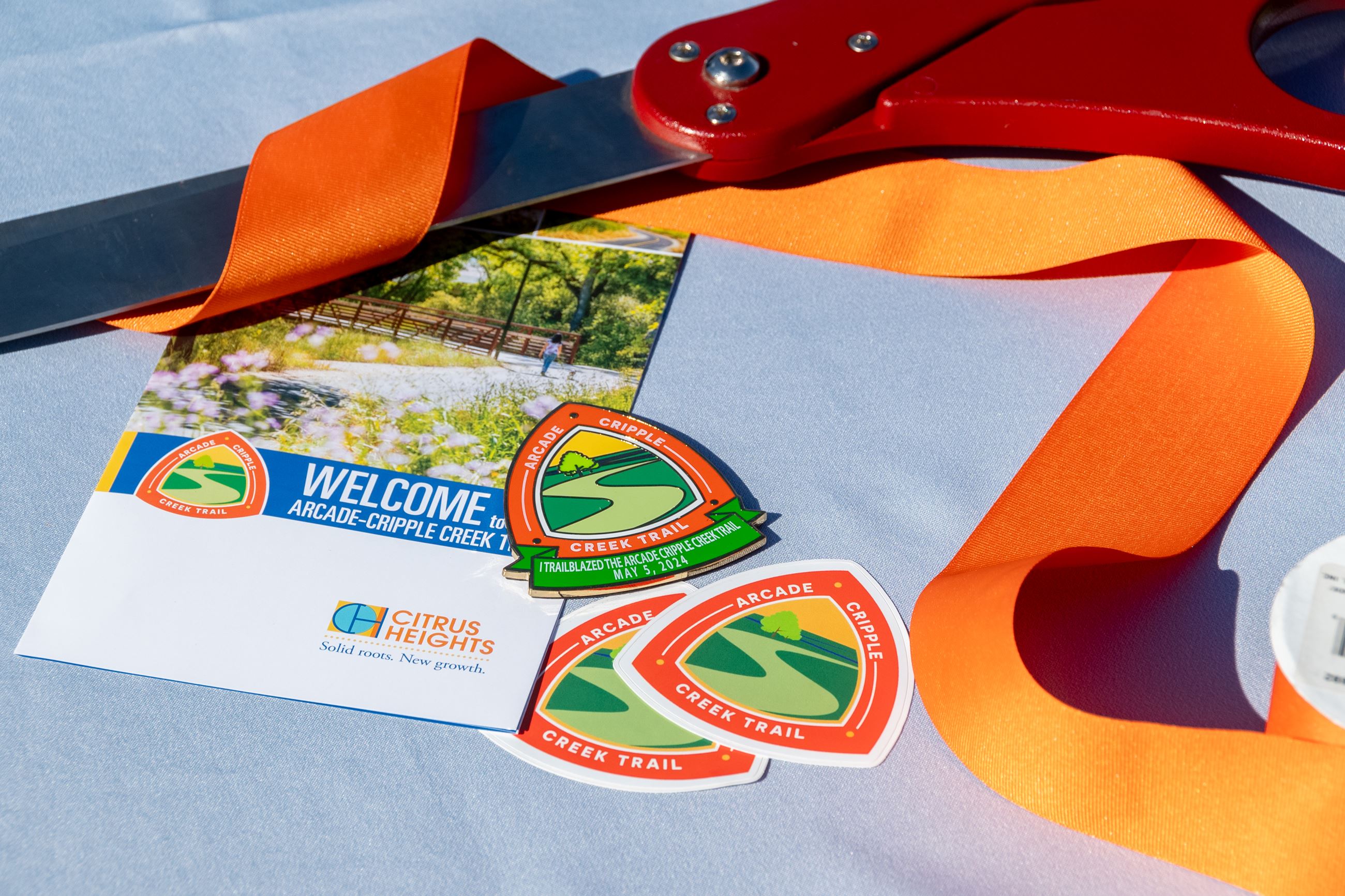 Logo sticker, brochure, ribbon and giant scissors on a table
