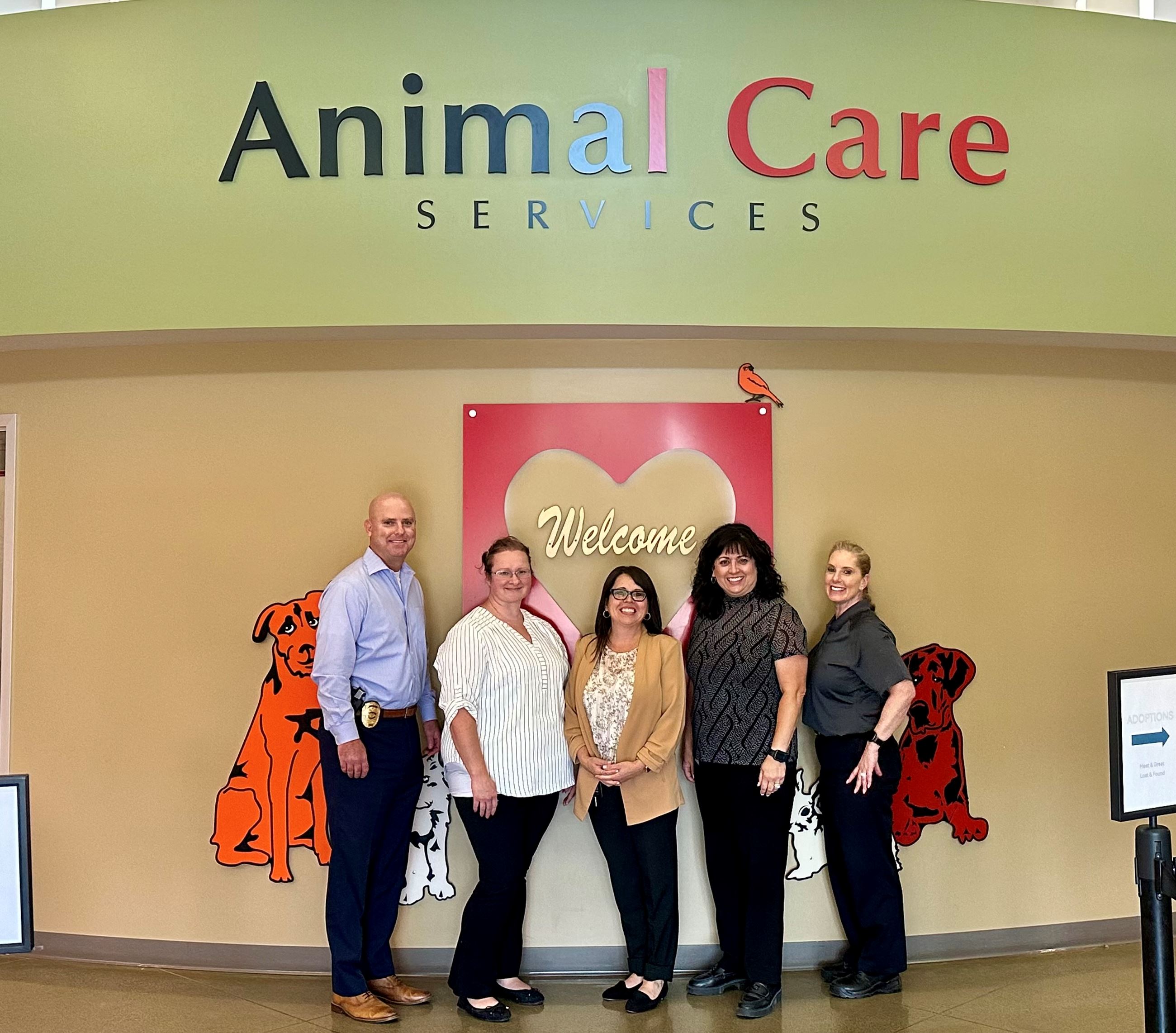 Five people pose for a photo in front of a wall that reads "Animal Care Services"