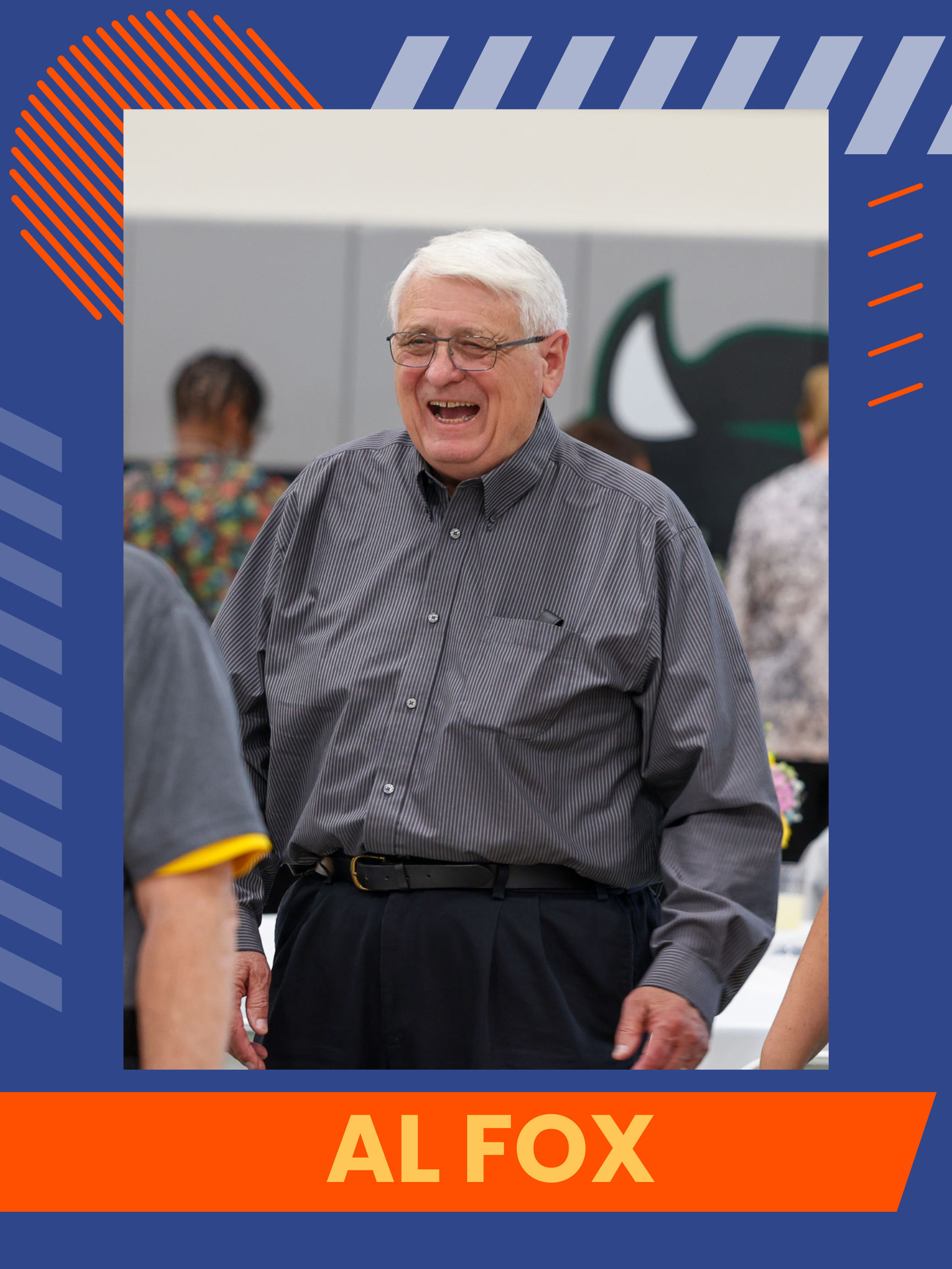 Al Fox, a man wearing a grey button up, black pants, and glasses. He's standing and smiling.